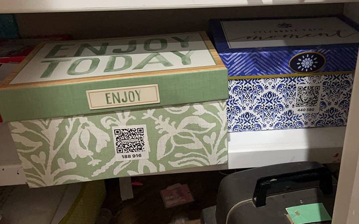 Two lidded storage boxes on a closet shelf, each with a QR code label on its side