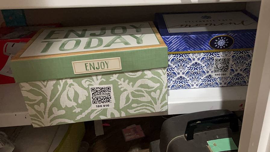 Two lidded storage boxes on a closet shelf, each with a QR code label on its side