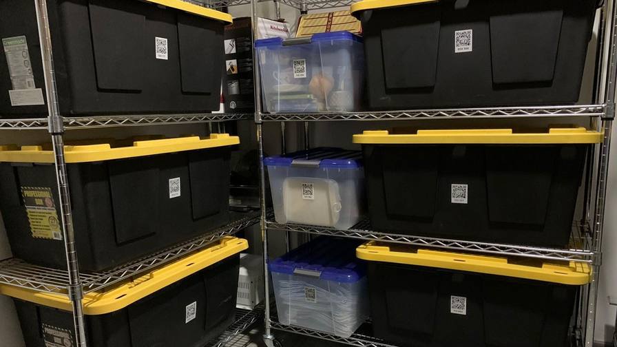 Plastic storage totes stacked on wire shelving, each with a QR code label on its side