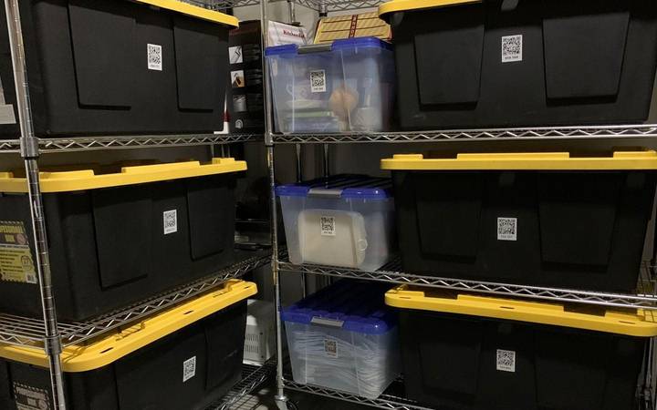 Plastic storage totes stacked on wire shelving, each with a QR code label on its side
