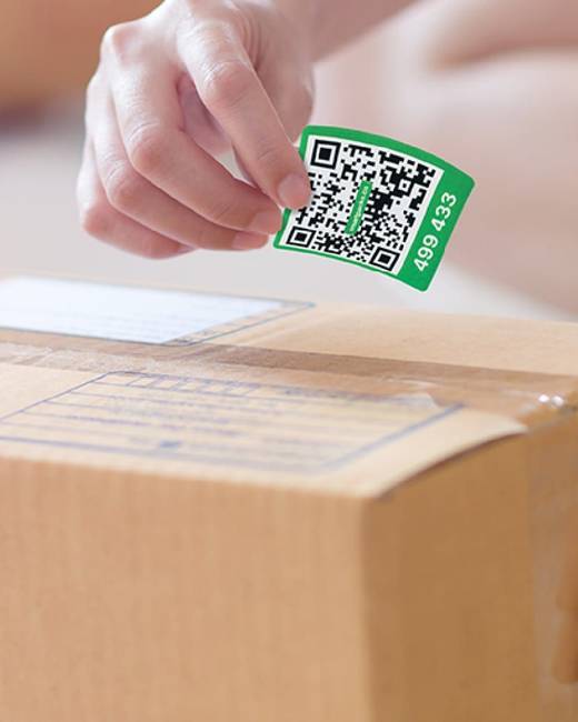A hand about to press a green SmartPacks QR label onto a sealed cardboard box