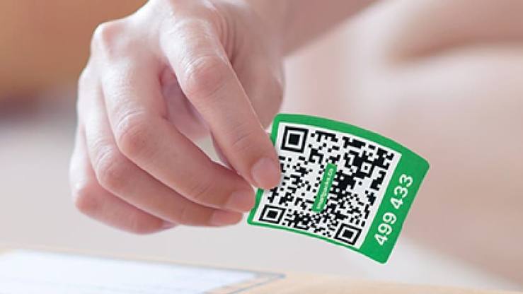 A hand about to press a green SmartPacks QR label onto a sealed cardboard box