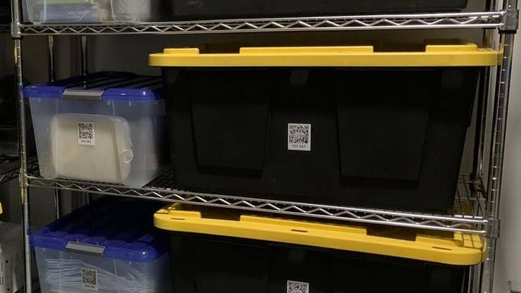 Metal shelving with black and clear storage bins, every bin carrying a SmartPacks QR label