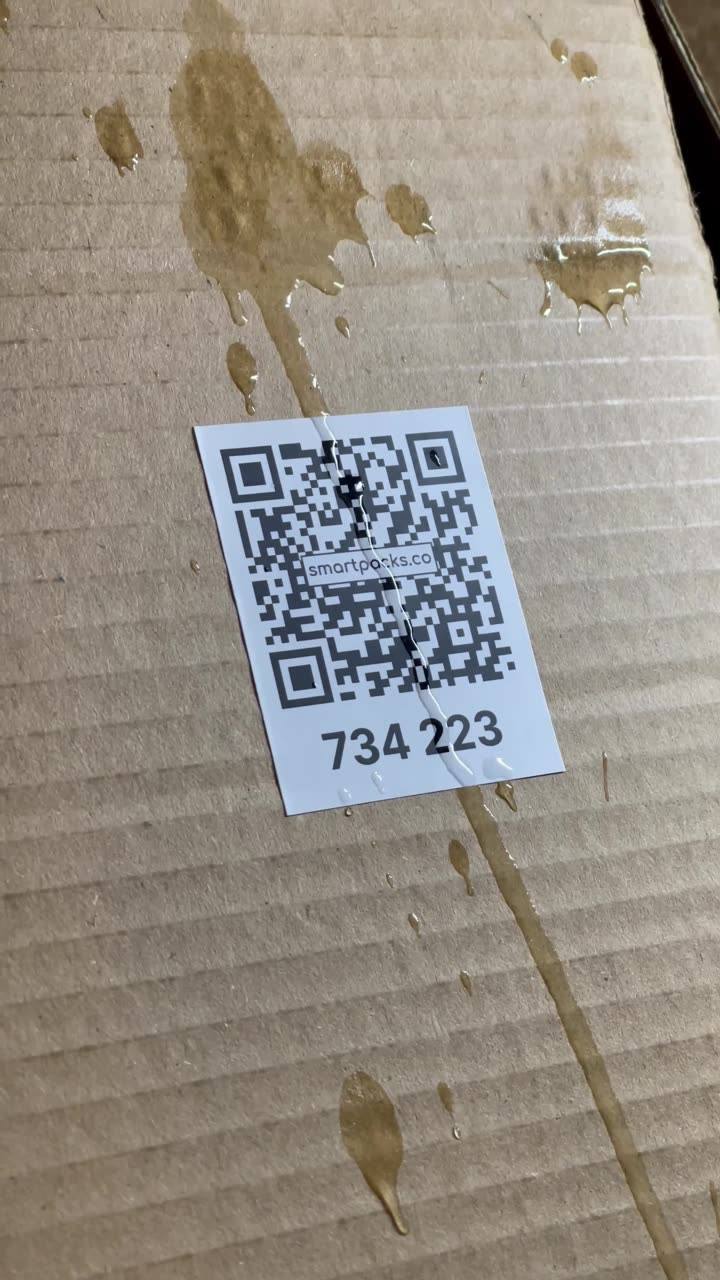A SmartPacks QR label stuck on a cardboard box with liquid running down over the code and the box